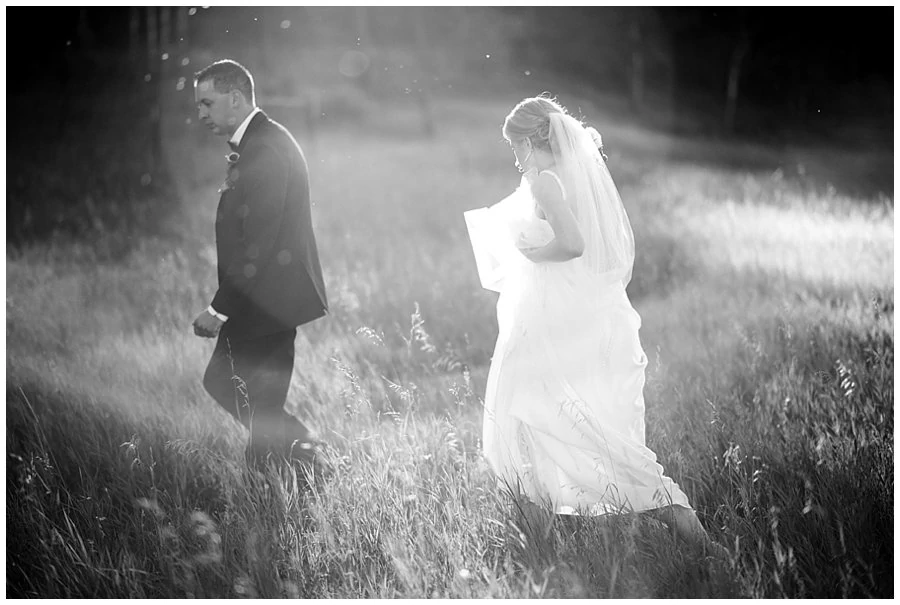 bride and groom walk in field at sunset at Deer Creek Valley Ranch wedding by Colorado wedding photographer Jennie Crate