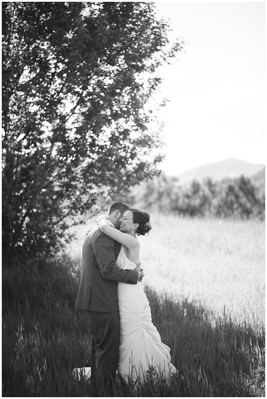 bride and groom embrace in field on wedding day at spring Denver Botanic Gardens at Chatfield Wedding by Denver Botanic Gardens wedding photographer Jennie Crate