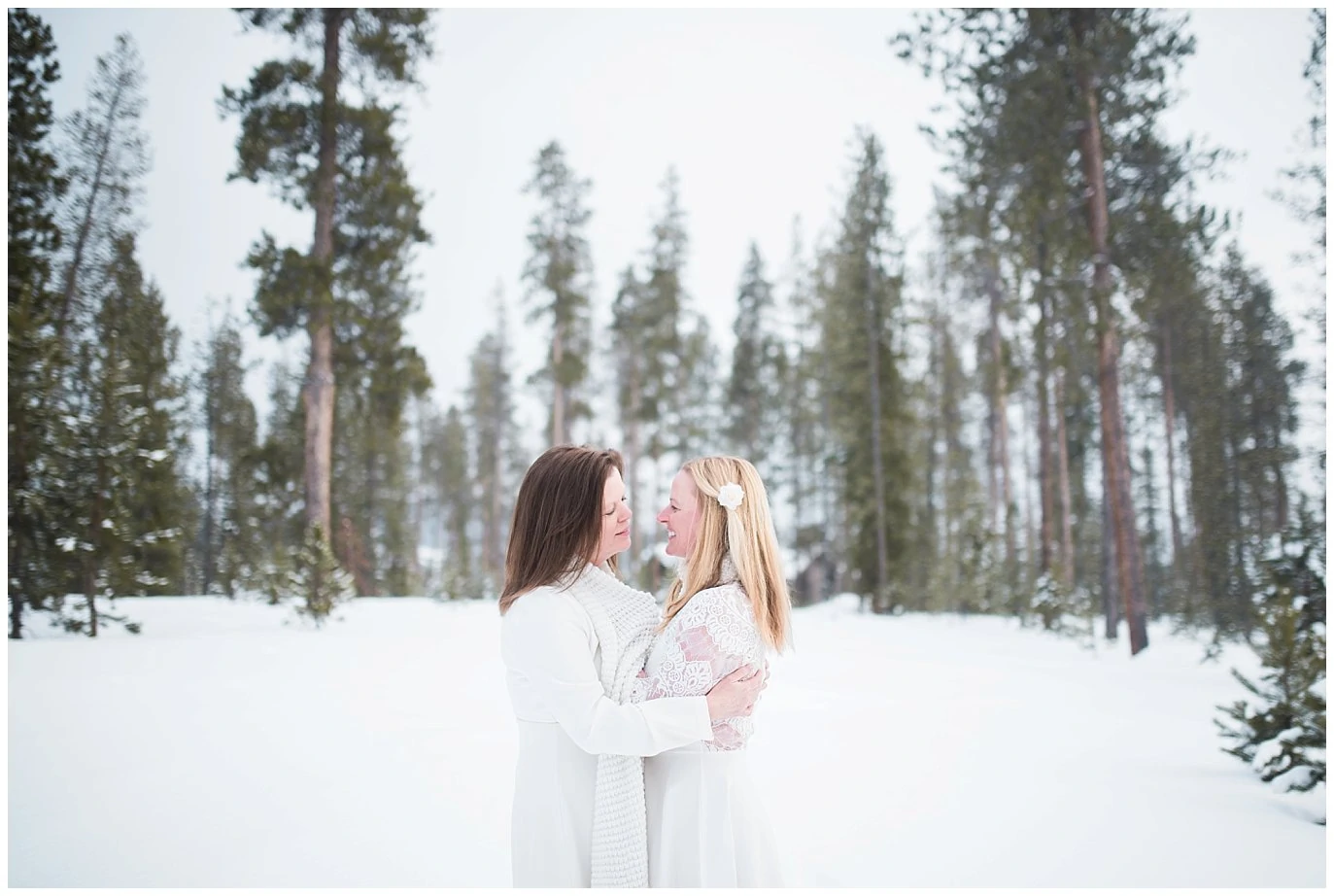 two brides cuddle in evergreen trees at Winter Devil's Thumb Ranch Elopement 