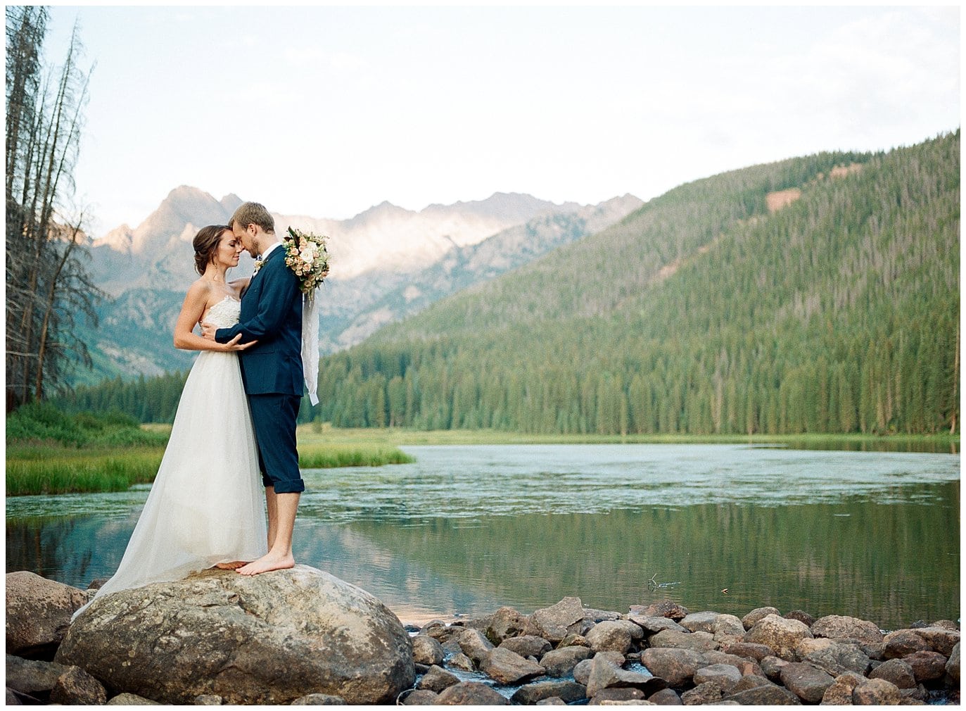 bride and groom on rocks by alpine lake during sunset at Piney River Ranch intimate wedding by Beaver Creek wedding photographer Jennie Crate Photographer