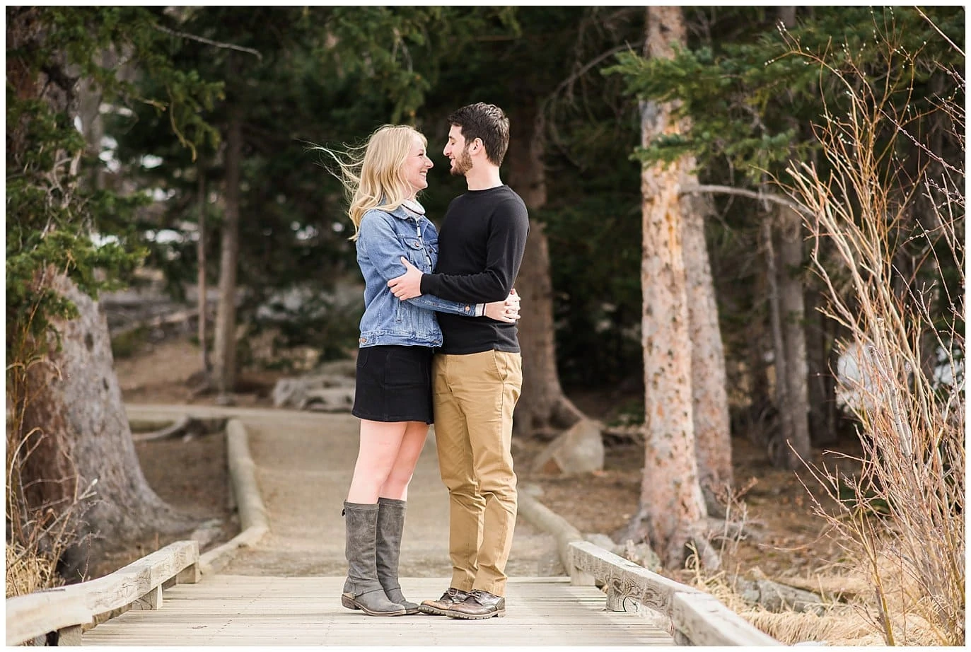 bride and groom in spring clothes hug on wooden bridge at sprague lake engagement session by Estes Park wedding photographer Jennie Crate
