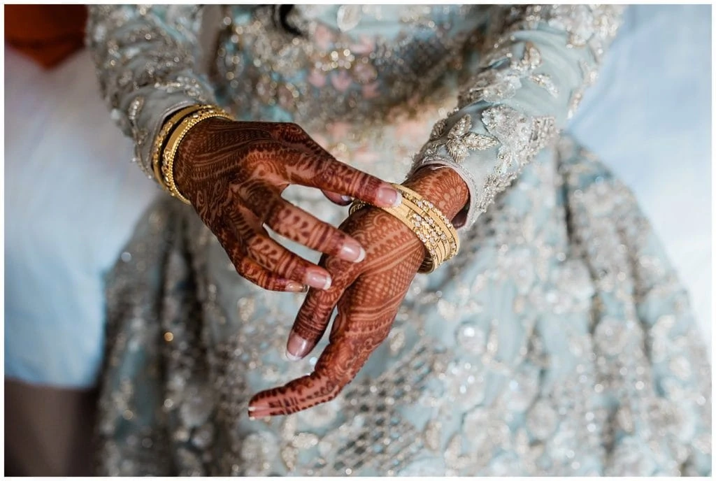 bride putting on gold bracelets with henna photo