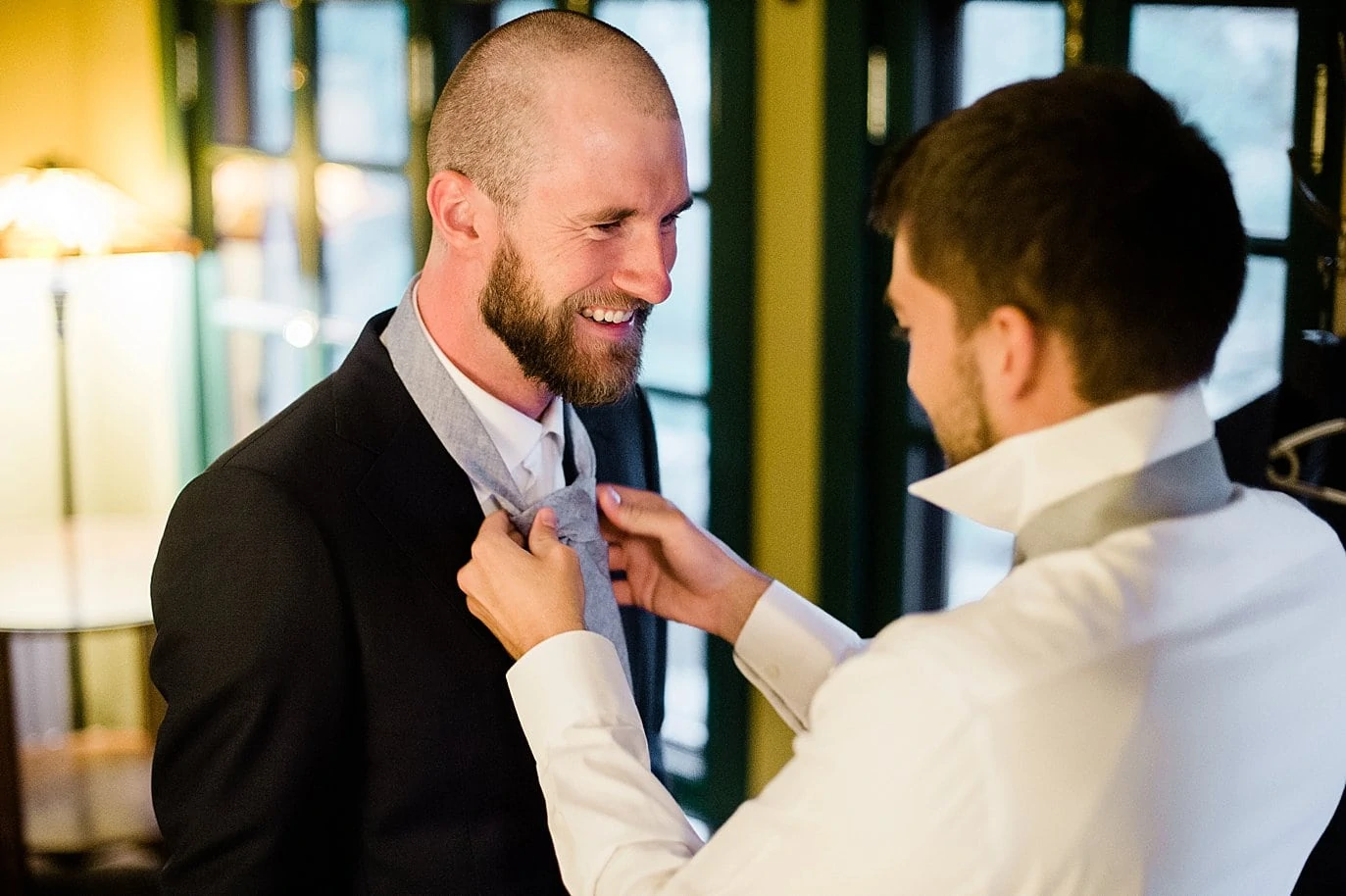 groomsman tying groom tie at golden wedding