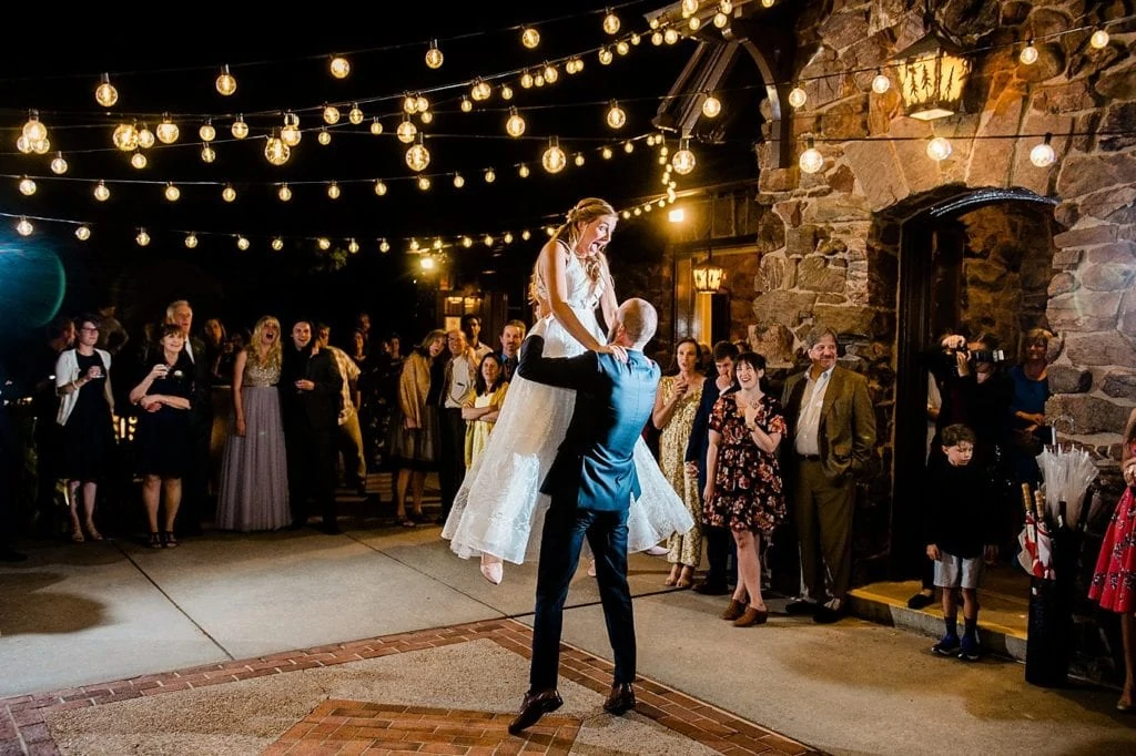 groom lifts bride during first dance on outdoor patio under the market lights