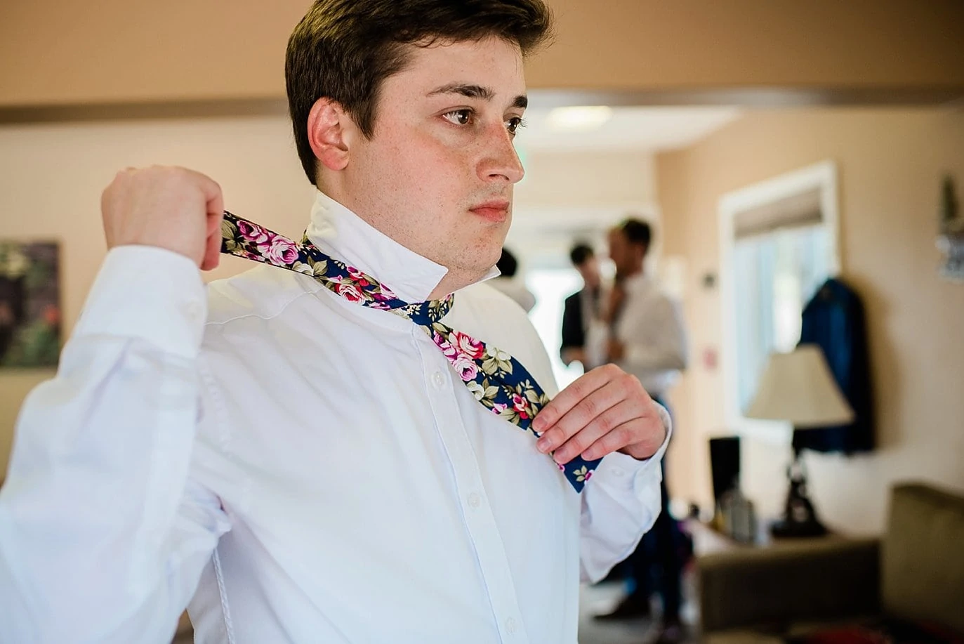 Groom tying floral bow tie on wedding day photo