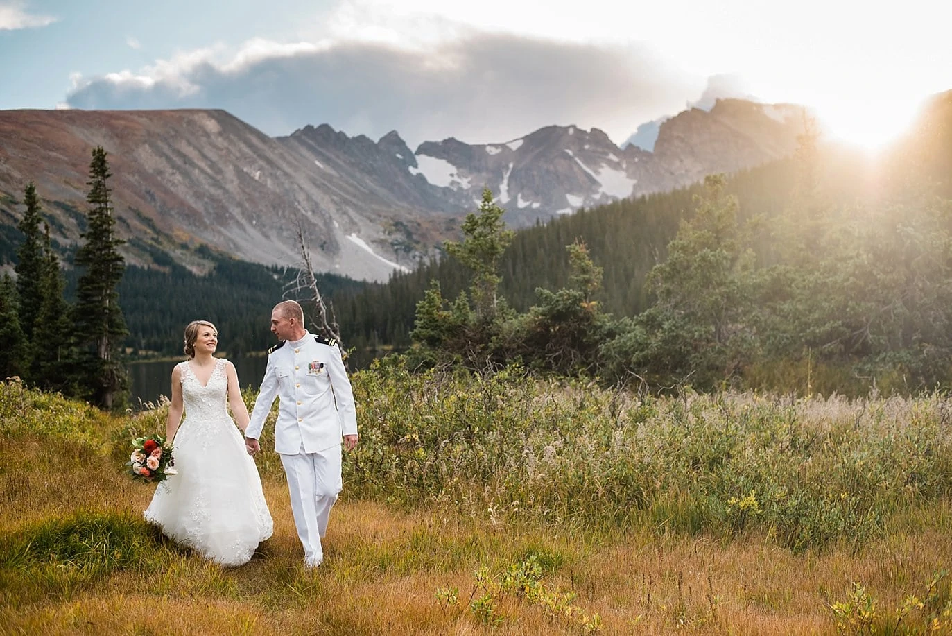 bride and groom walk in field with view of colorado mountains