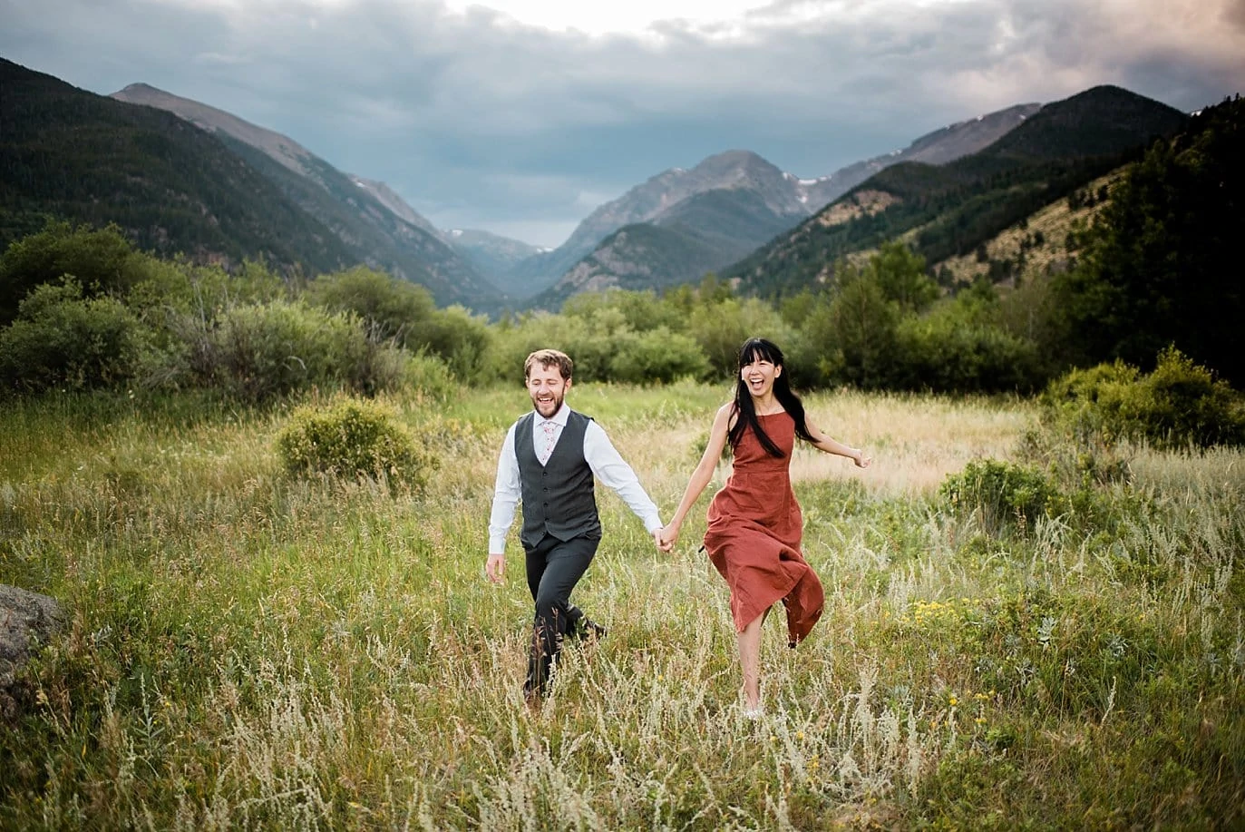 engaged couple running through the National Park in Colorado at Lawn Lake Trailhead Engagement