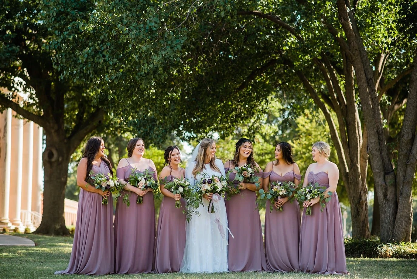 bride and bridesmaids in lavender dresses in trees of First Christian Church Wichita Falls wedding