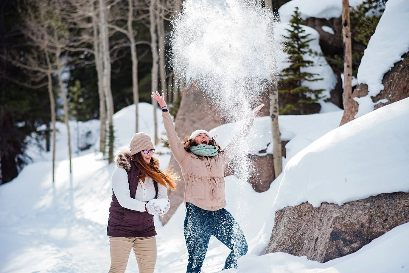 same-sex couple plays in snow Alberta Falls Rocky Mountain National Park winter hiking engagement by Rocky Mountain engagement photographer Jennie Crate, Photographer