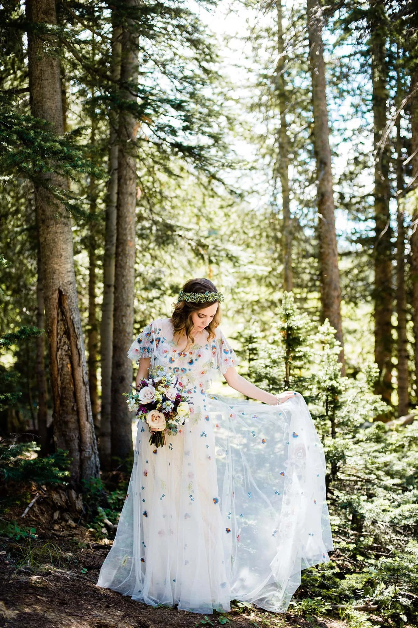 bride in unique floral chiffon wedding dress in sunlight in trees at Arapahoe Basin wedding by Frisco wedding photographer Jennie Crate