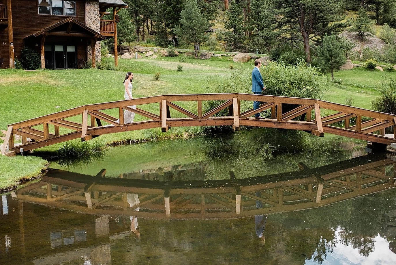 bride approaches groom for first look on bridge over pond at Black Canyon Inn wedding by Denver wedding photographer Jennie Crate Photographer