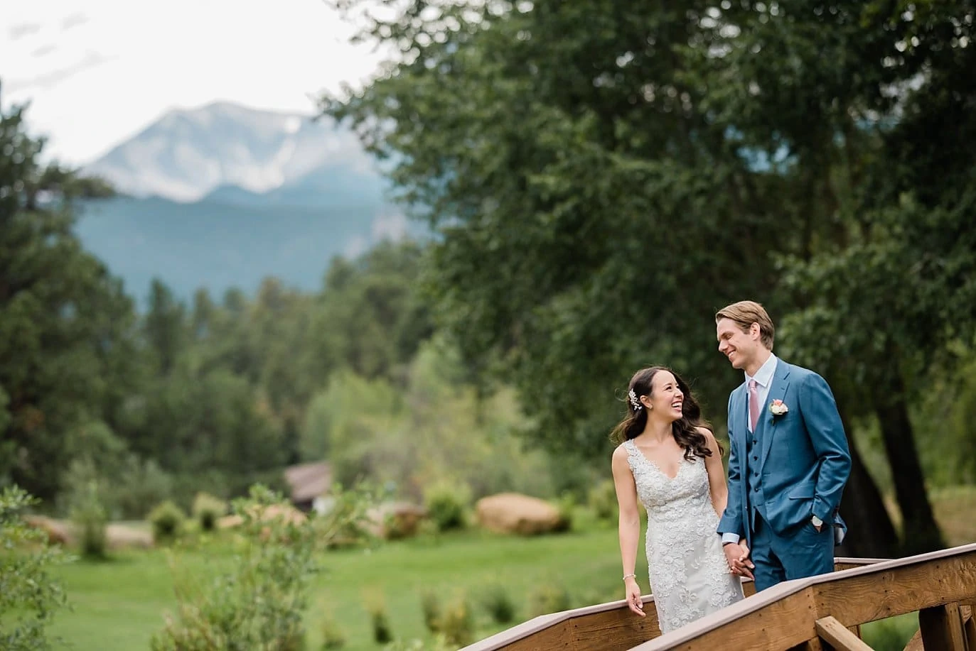 bride and groom on bridge over pond in front of mountains at Black Canyon Inn wedding by Estes Park wedding photographer Jennie Crate Photographer