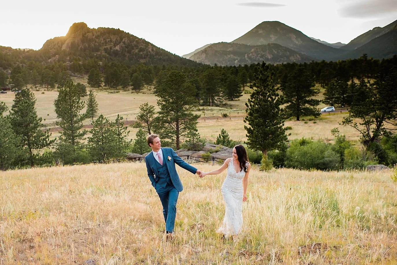 bride and groom walk across field in Estes Park at sunset at t Twin Owls Steakhouse wedding by RMNP wedding photographer Jennie Crate photographer