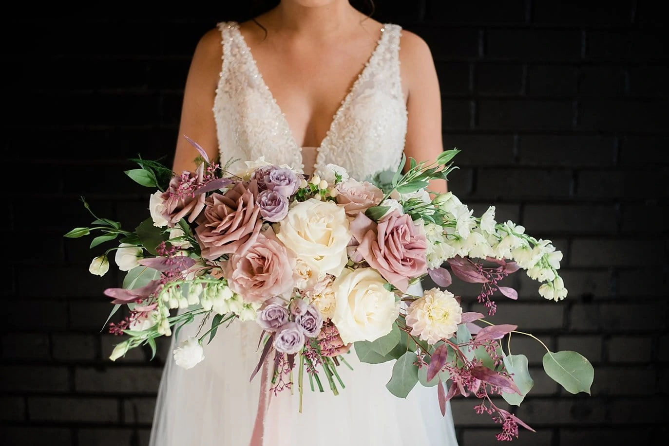 bride with large lavender and rose bridal bouquet in front of black brick wall at at Shyft Denver wedding by Denver wedding photographer Jennie Crate photographer