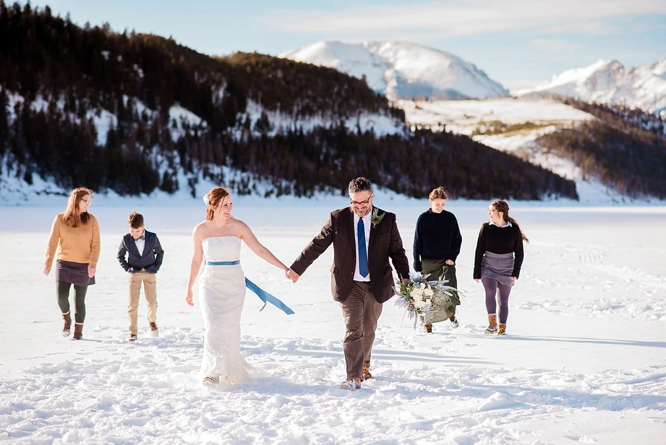 bride and groom walk across frozen lake dillon with kids at Sapphire Point Elopement by Vail wedding photographer Jennie Crate Photographer