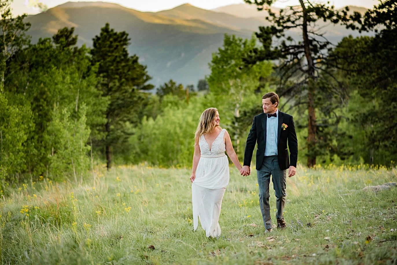 bride and groom walk hand in hand in field with mountain alpenglow at Golden elopement by Golden elopement photographer Jennie Crate