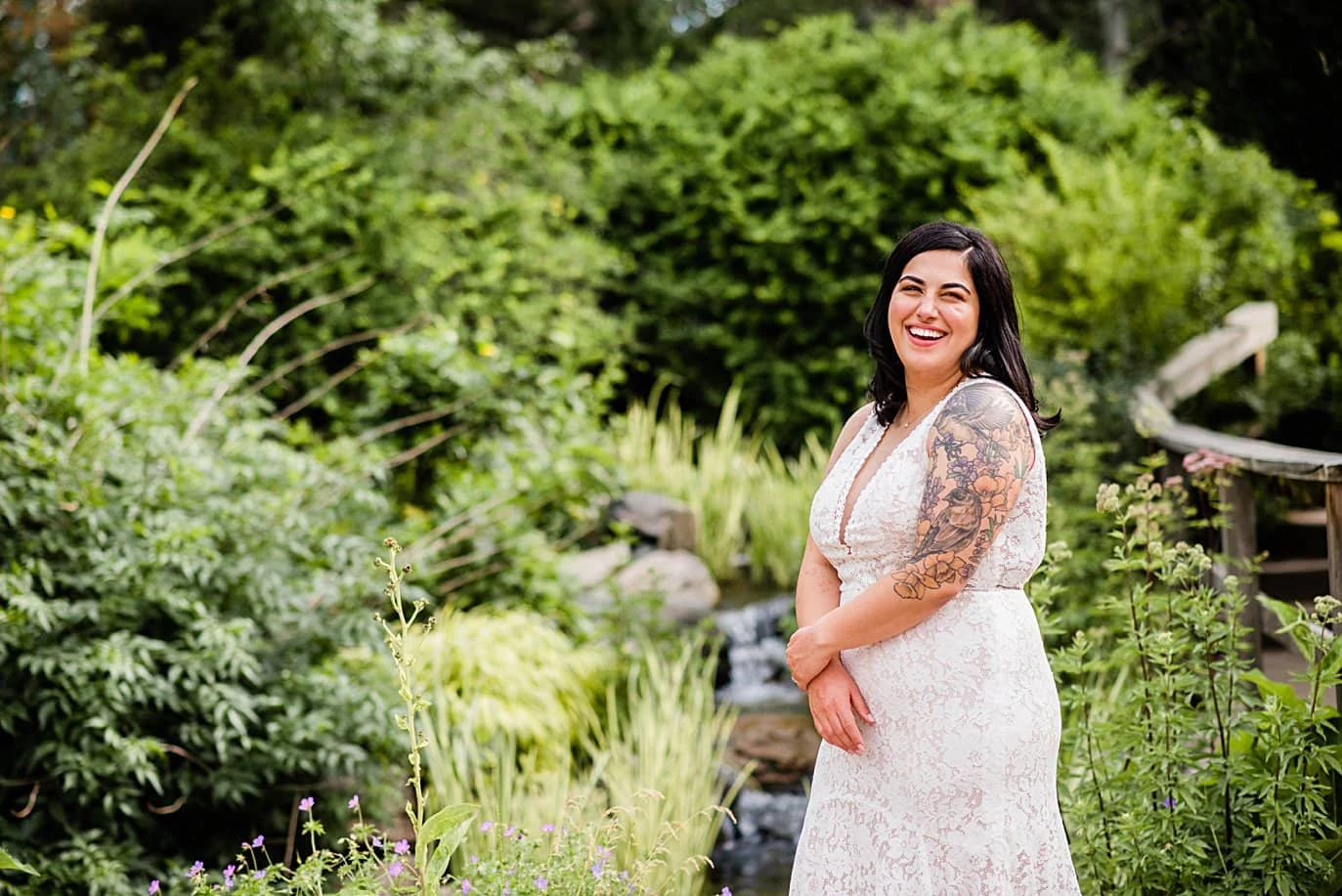 bride in lace dress with tattoos by creek at Denver Botanic Gardens wedding by Boulder Wedding Photographer Jennie Crate