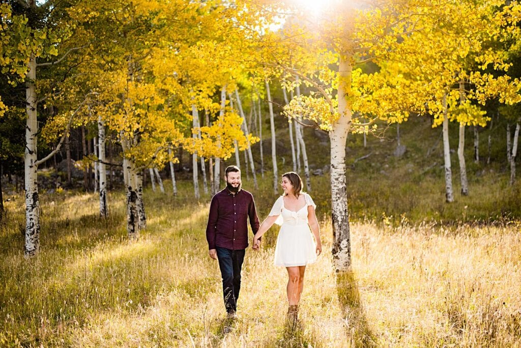couple walks in sunshine in golden aspen grove at RMNP engagement session by Boudler engagement photographer Jennie Crate