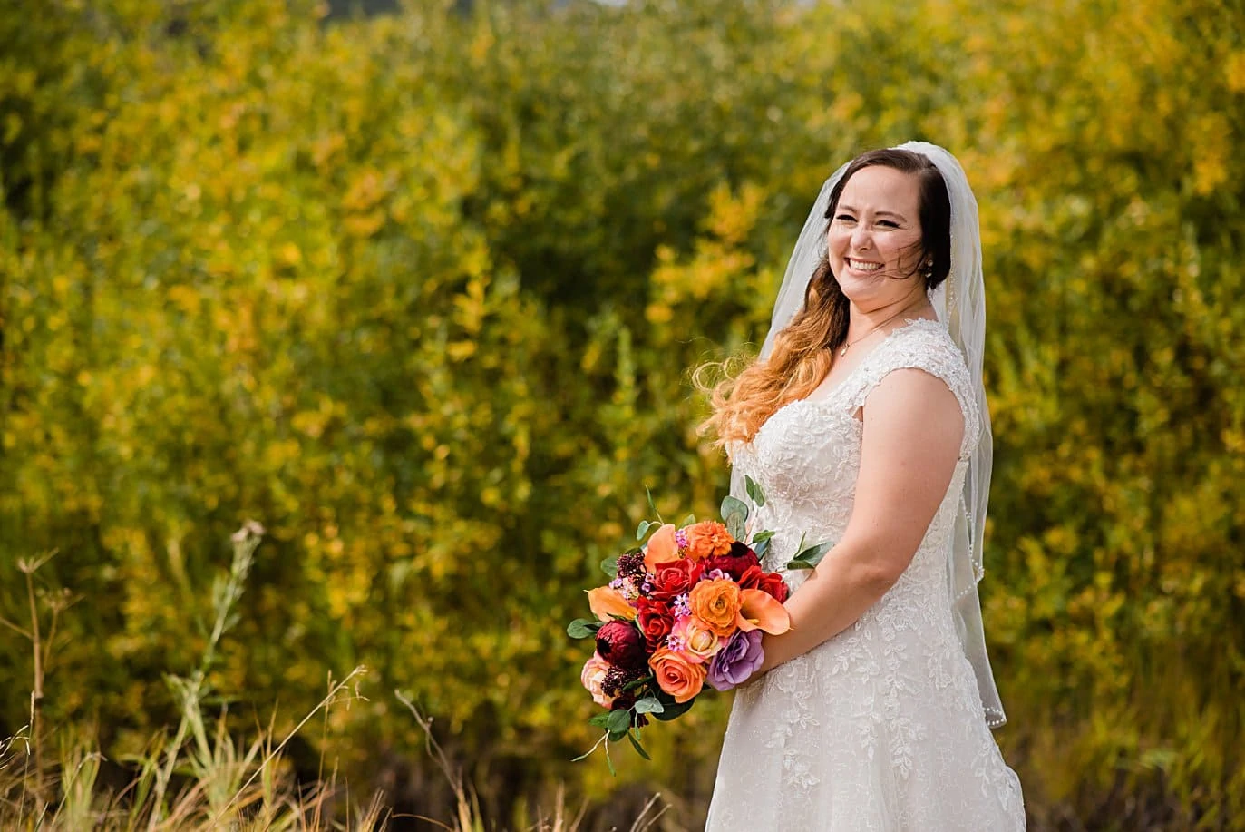bride with colorful flowers in fall foliage at Deer Creek Valley Ranch wedding by Conifer wedding photographer Jennie Crate