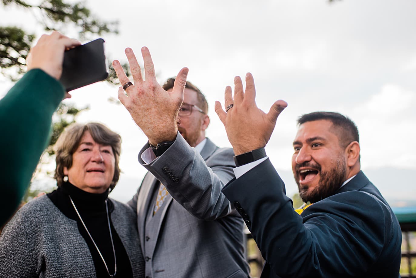 grooms show off wedding rings to guest on zoom at Panorama point during LGBTQ wedding by Colorado LGBT photographer Jennie Crate