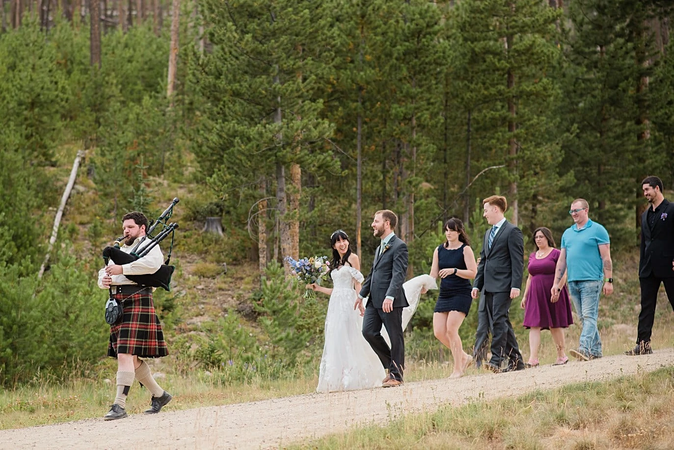 bride and groom walk with friends to wedding ceremony with bagpiper leading the way at intimate Grand Lake wedding by Denver wedding photographer Jennie Crate