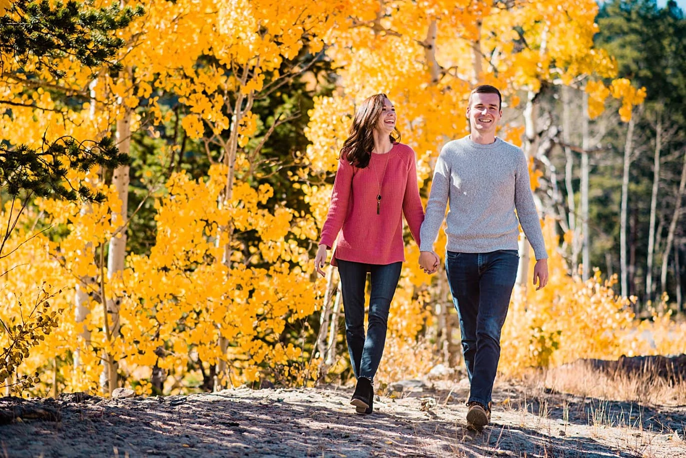 couple walks hand in hand in front of yellow aspens during fall engagement session in Ward Colorado by Boulder engagement photographer Jennie Crate