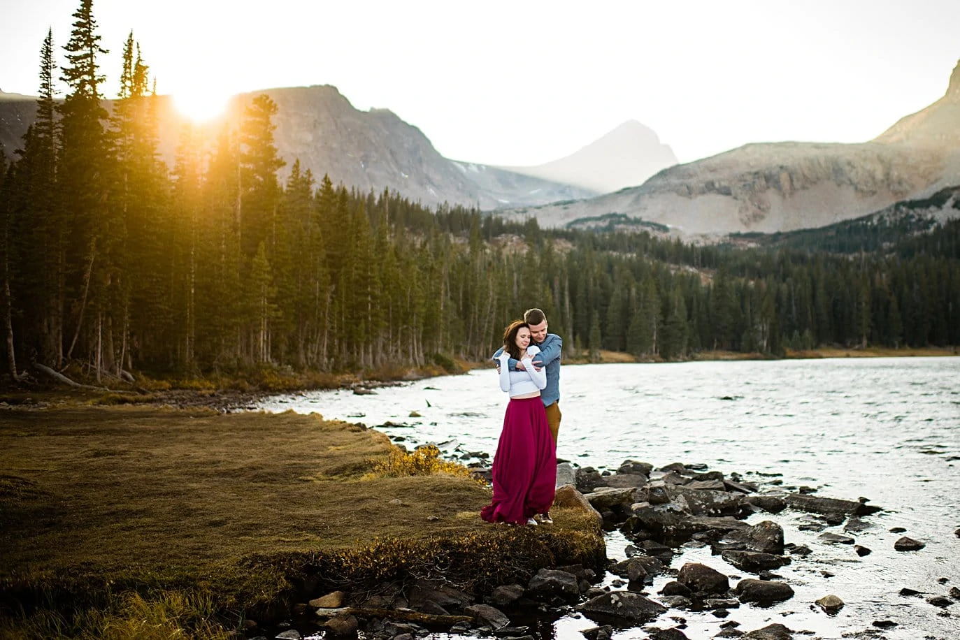 sunset engagement at Mitchell Lake as sun peeps over peaks with couple in colorful attire by Denver engagement photographer Jennie Crate