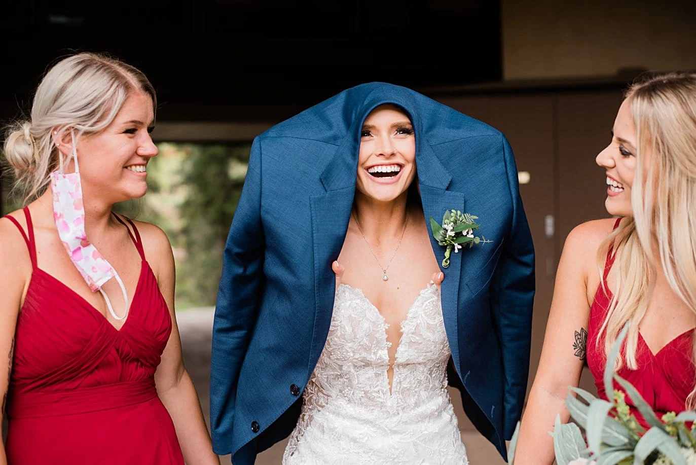 Bride shelters from rain under groom's coat while bridesmaids in masks look on at Vail Manor Lodge wedding by Aspen wedding photographer Jennie Crate