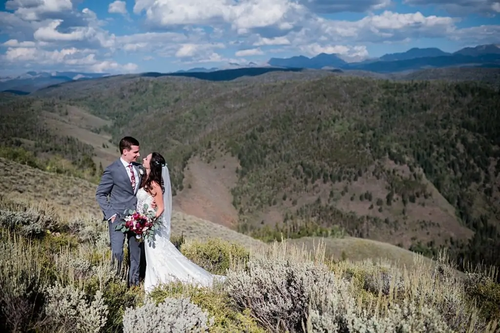bride and groom take portraits at top of mountain overlooking valley on hot fall day