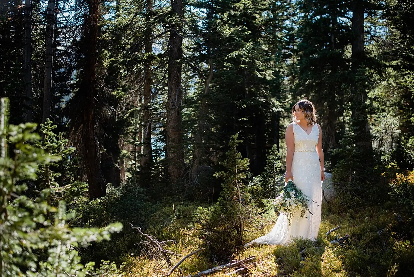bride in evergreen trees in lace dress during her long lake elopement