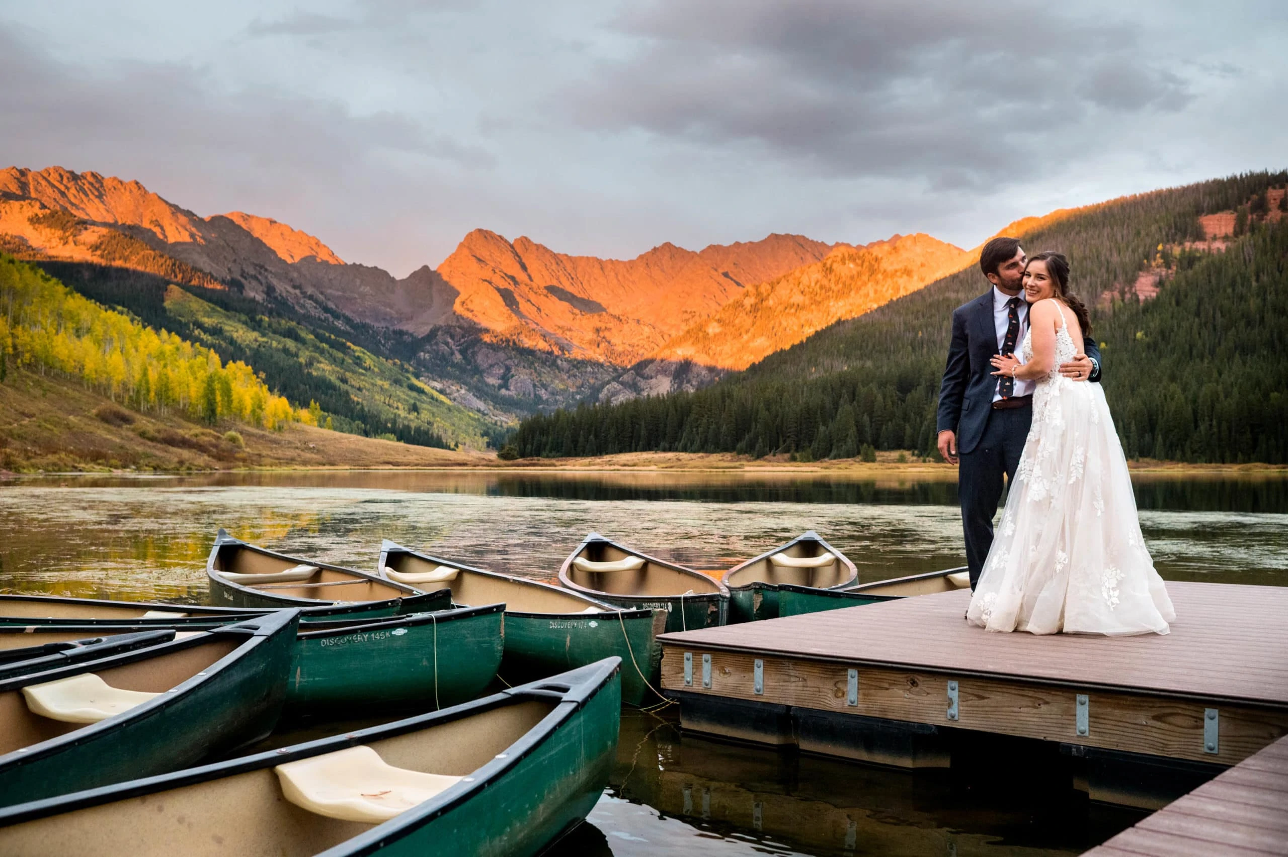 couple snuggles on dock with canoes at piney river ranch wedding