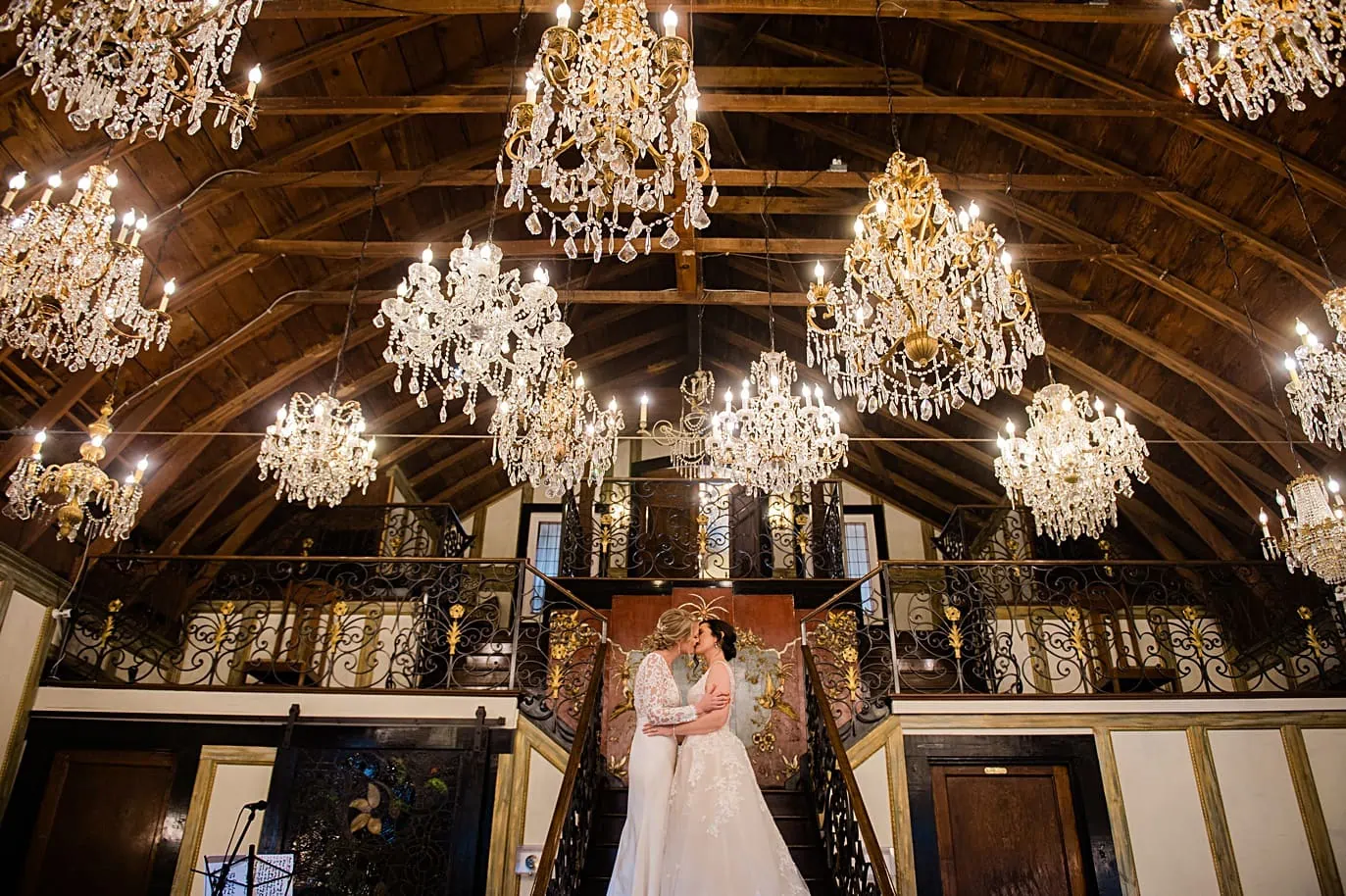 two brides kiss on the stairs after their wedding in the chandelier barn at the Lionsgate Event Center