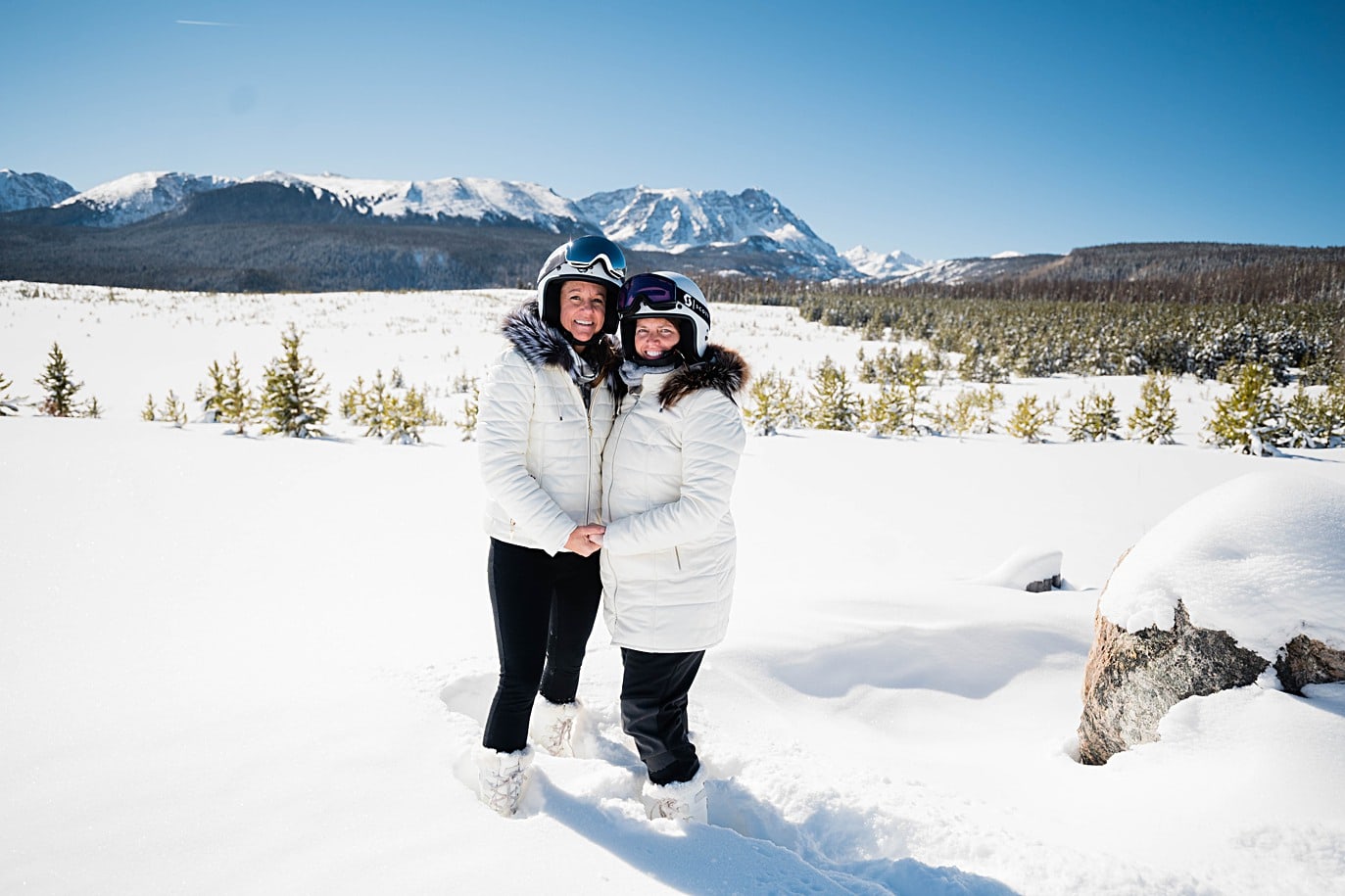Two brides at Breckenridge Snowmobile elopement with snowcapped mountains behind them